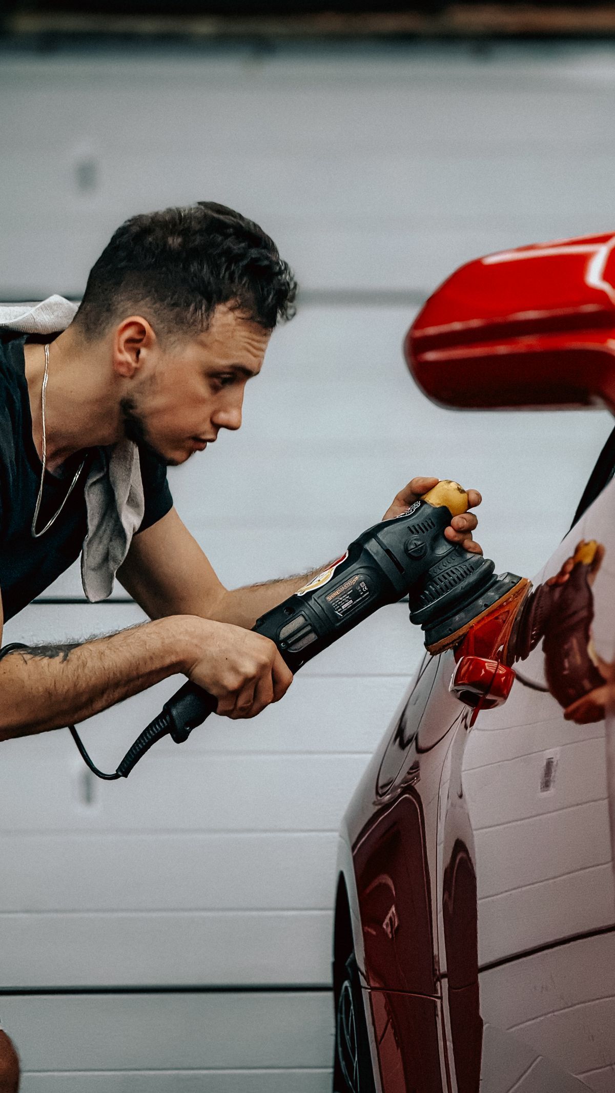 Detailer hand-polishing a red car's paintwork in a garage